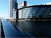 在蔚蓝的天空下，曼彻斯特的摩天大楼与海滨建筑的倒影清晰可见