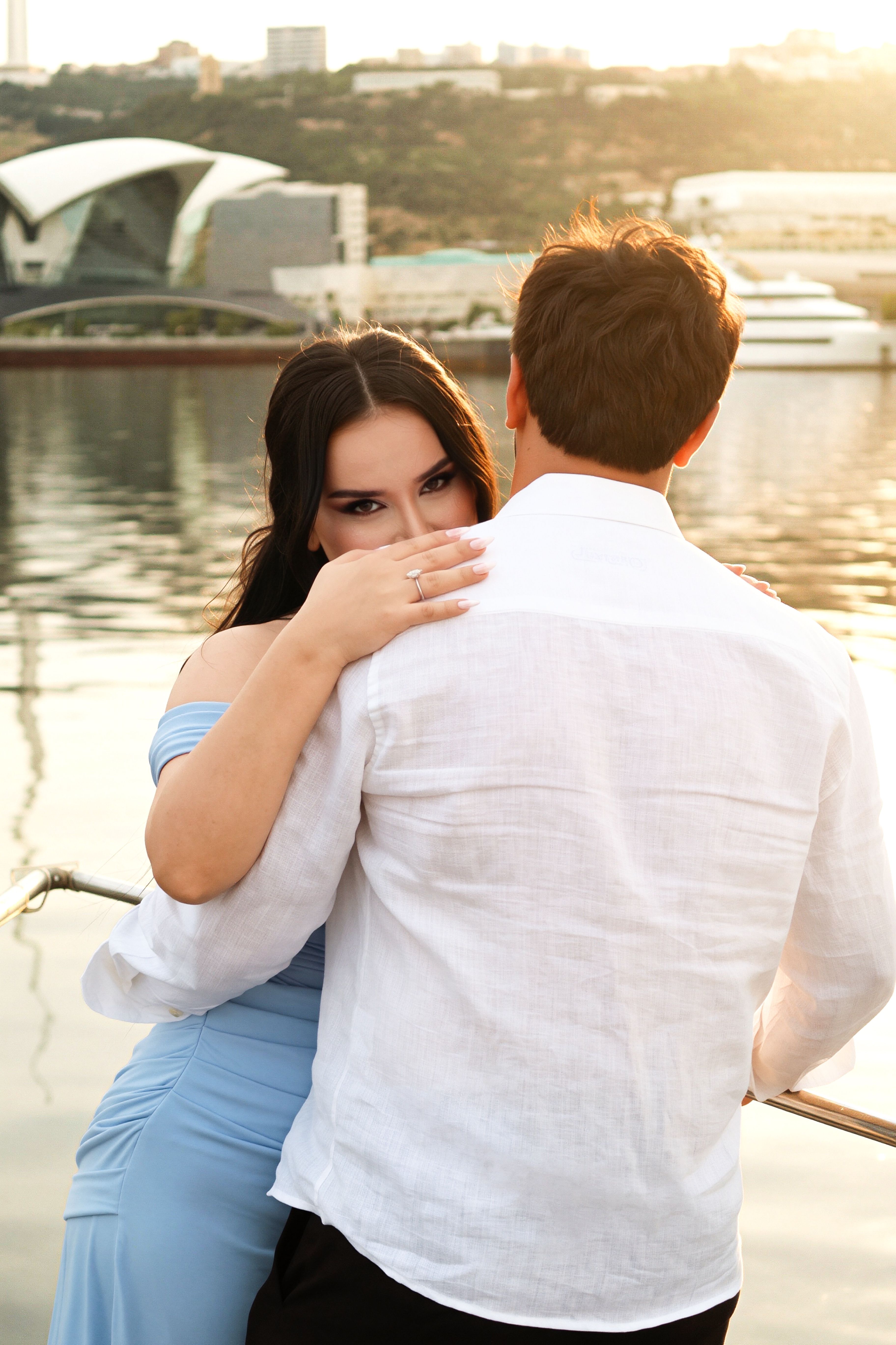 Couple embraces on a boat with Baku skyline at sunset, capturing romantic vibes.