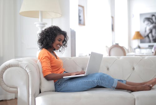 Free Smiling African American woman browsing laptop on couch Stock Photo