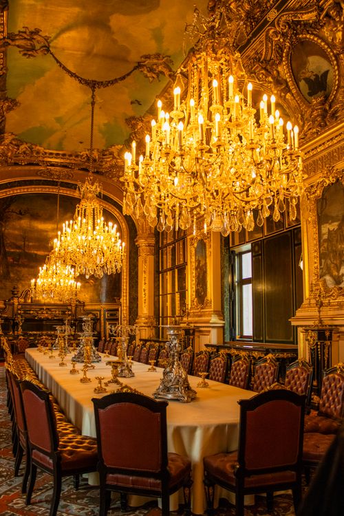 Free Opulent dining hall featuring grand chandeliers, elegant decor, and a long ornate table setting. Stock Photo