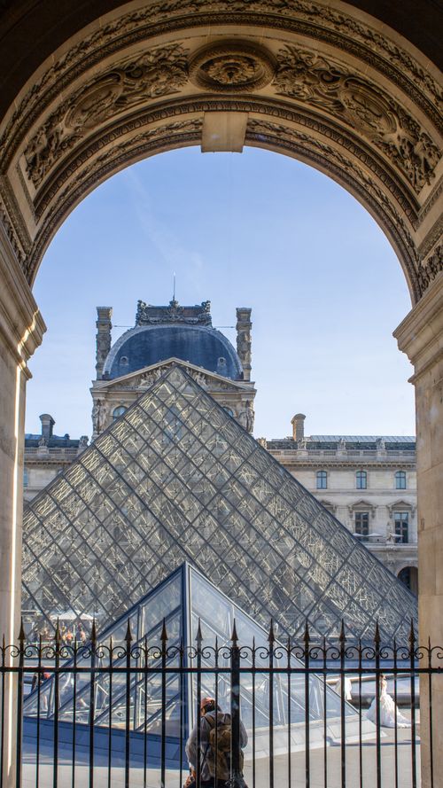Free Iconic glass pyramid viewed through historic arch at the Louvre Museum, Paris. Stock Photo