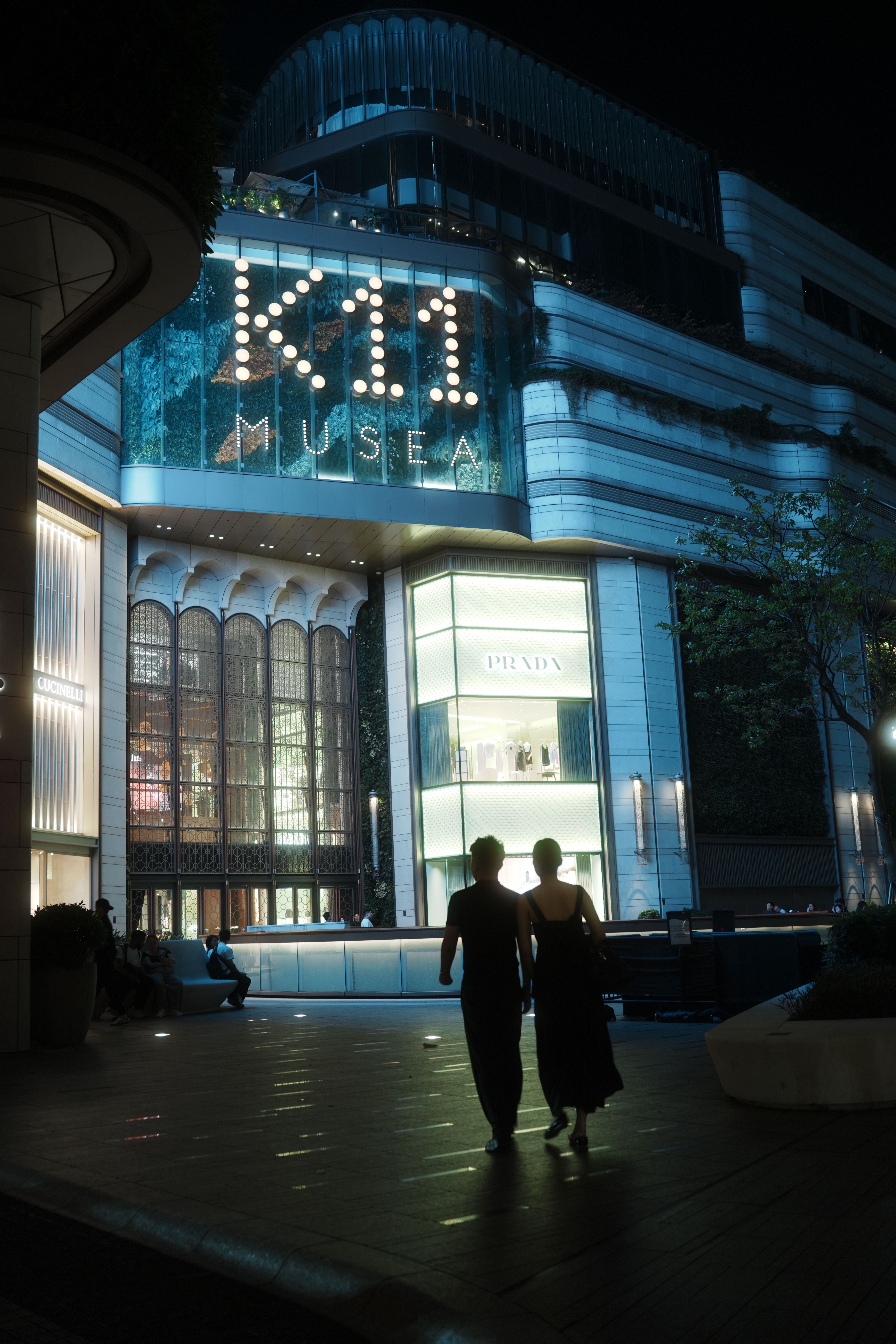 Silhouettes of people walking at night by K11 Musea, Hong Kong's shopping and cultural hub.