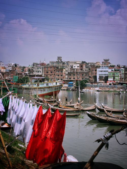 Free Vibrant river scene with boats and drying fabrics in a bustling Bangladeshi cityscape. Stock Photo