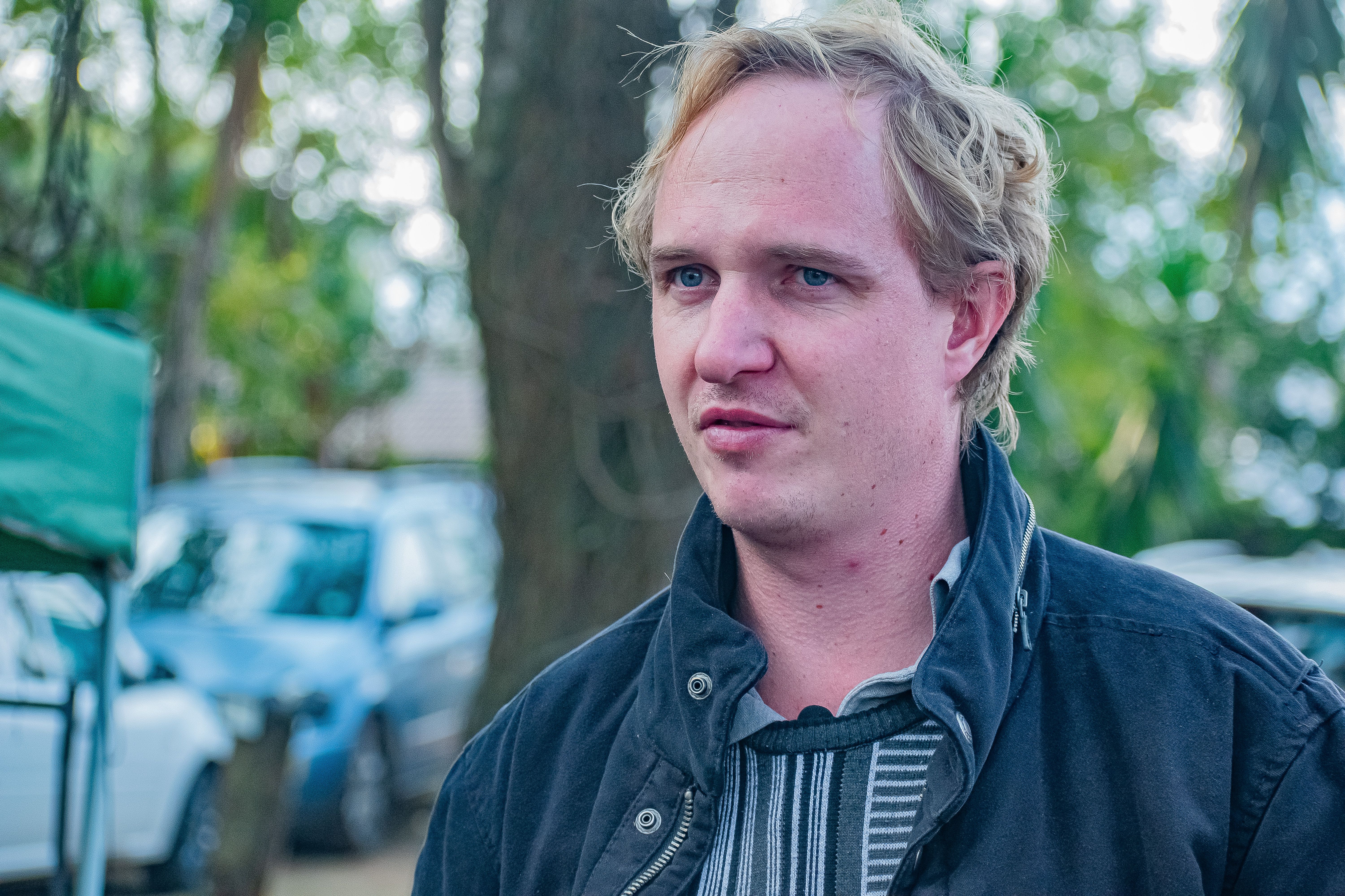Casual portrait of a man in Malkerns, surrounded by nature and parked cars.