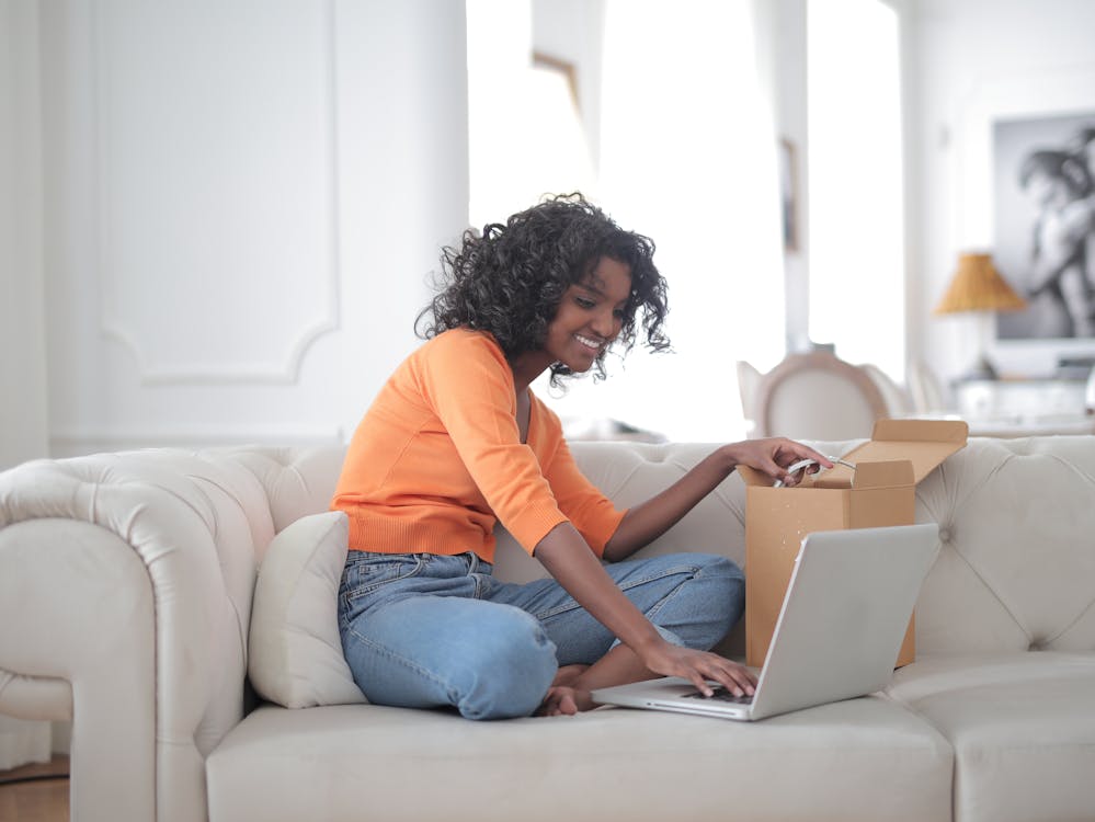 Cheerful black woman opening box and using laptop