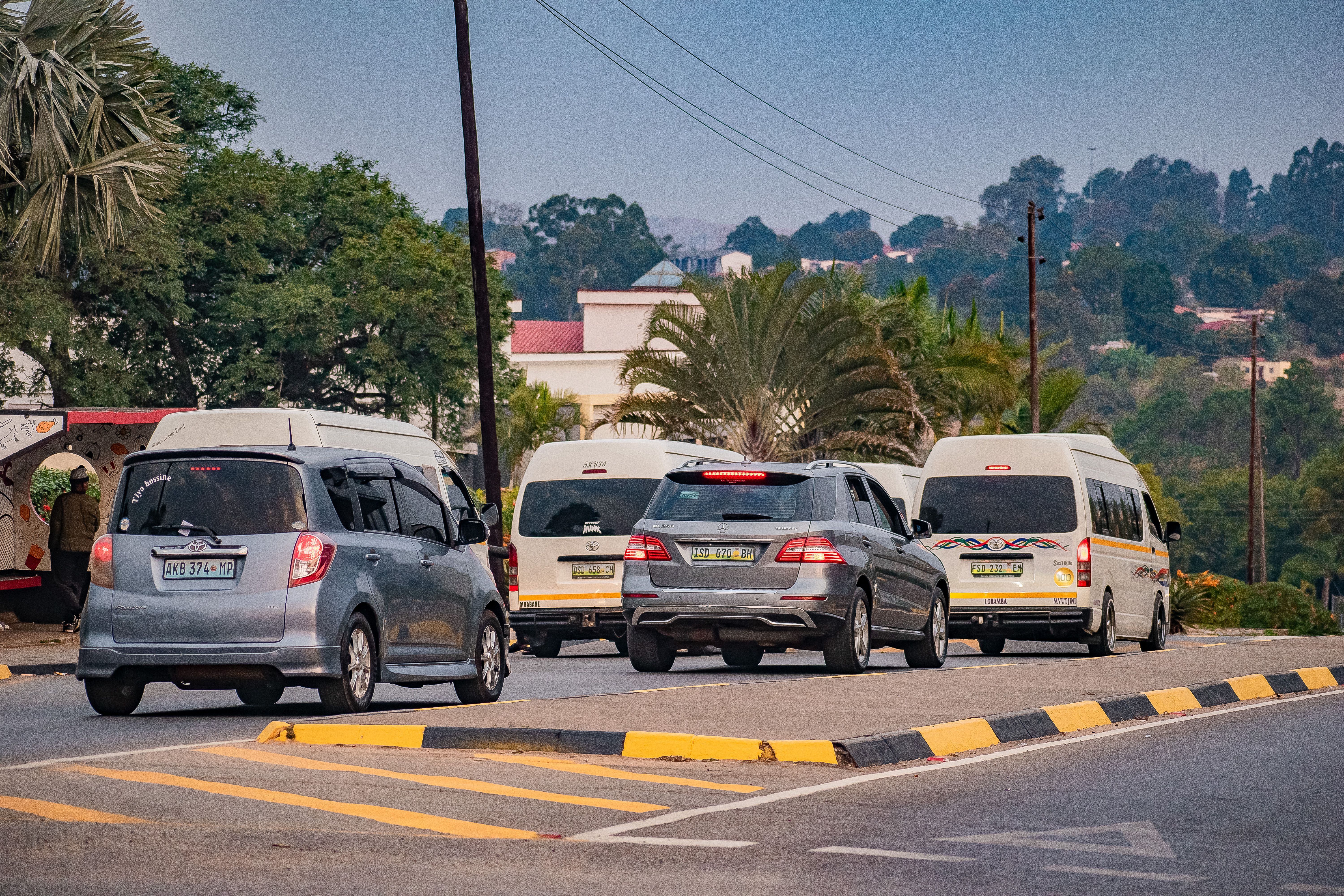 Street scene in Malkerns, Eswatini, with cars and vans lined along the road.