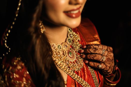 Close-up of a bride showcasing gold jewelry and detailed henna designs on a sunny day.
