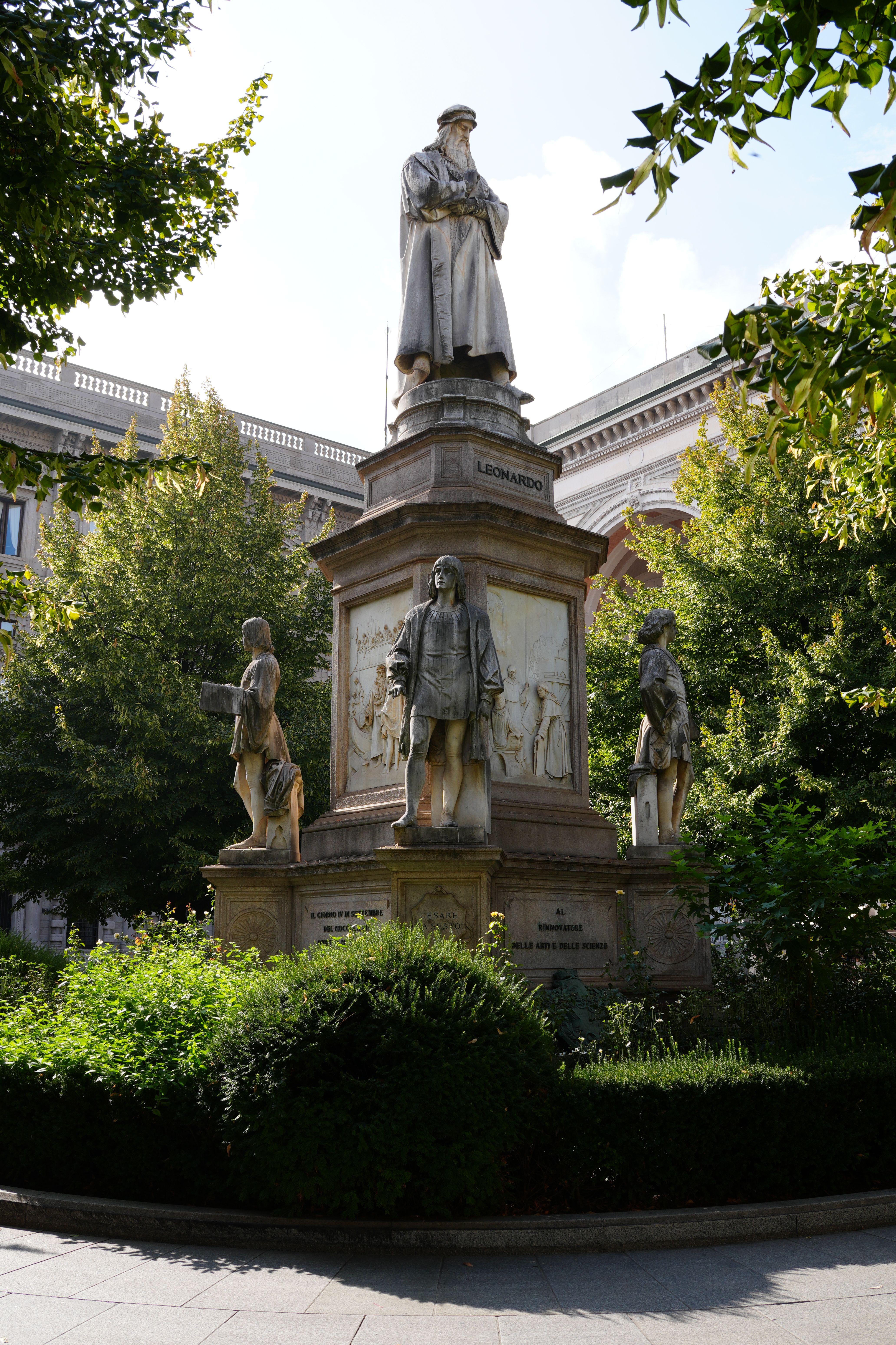 A majestic view of the Leonardo da Vinci statue in Piazza della Scala, Milan, surrounded by greenery.