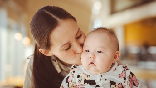 Free A mother lovingly kisses her baby on the cheek, capturing a tender moment indoors. Stock Photo