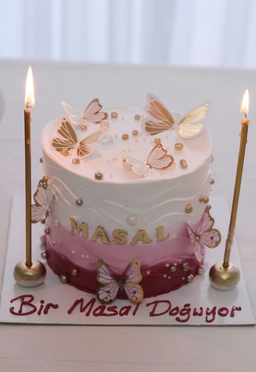 Free A beautiful pink and white cake adorned with butterfly decorations and golden accents, perfect for celebrations. Stock Photo