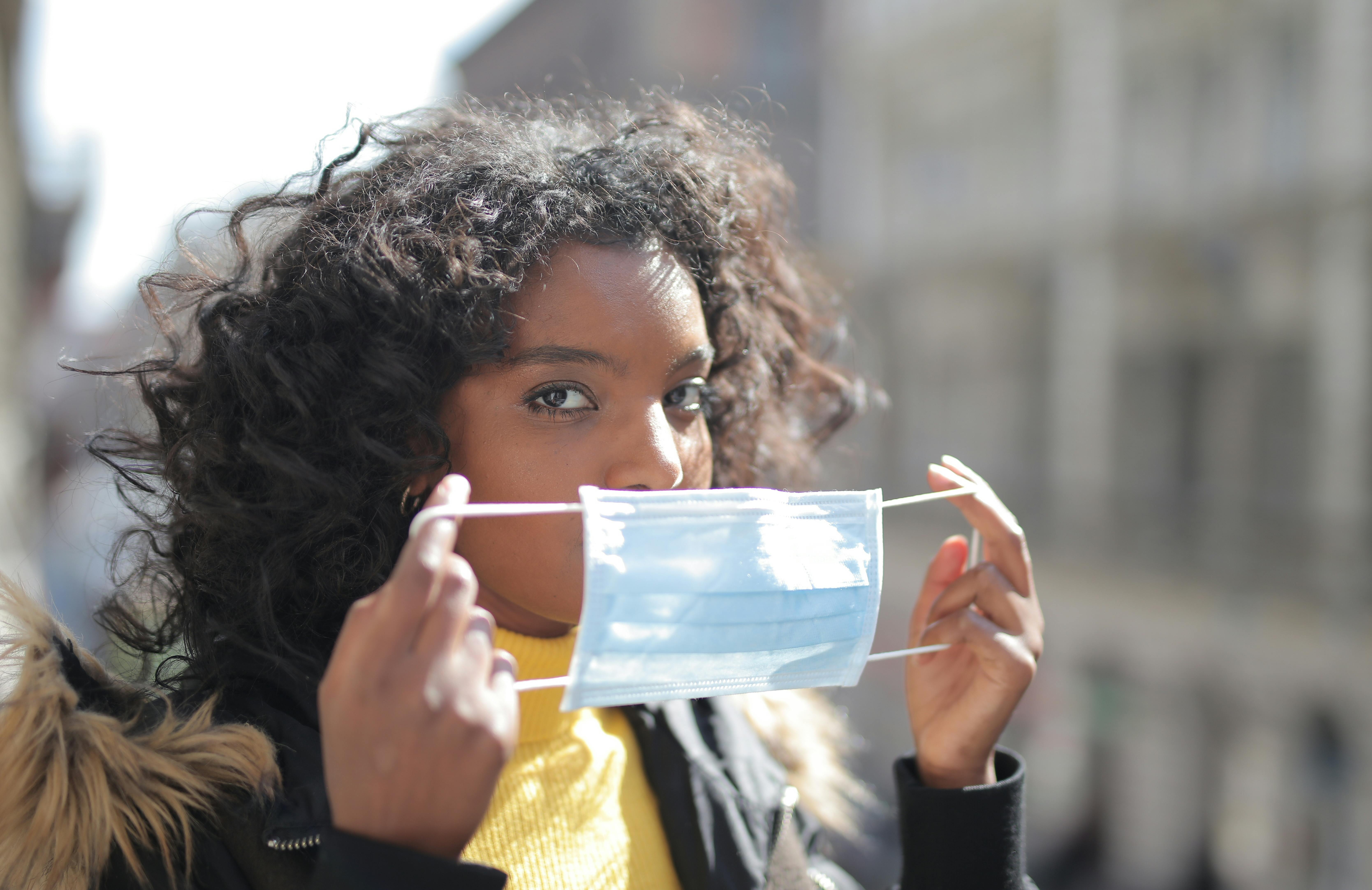Focused young ethnic lady putting on medical mask on street