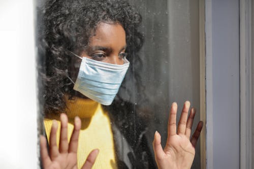 Free Serious young ethnic lady in medical mask standing near window and looking away on street Stock Photo