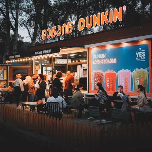Free Vibrant evening gathering outside Dunkin' store with people enjoying snacks and drinks. Stock Photo