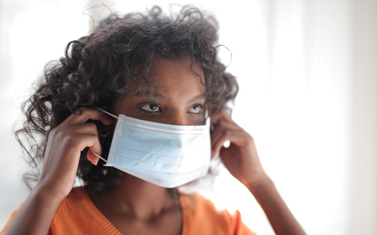 Young woman indoors adjusting a blue medical face mask, emphasizing healthcare and protection.