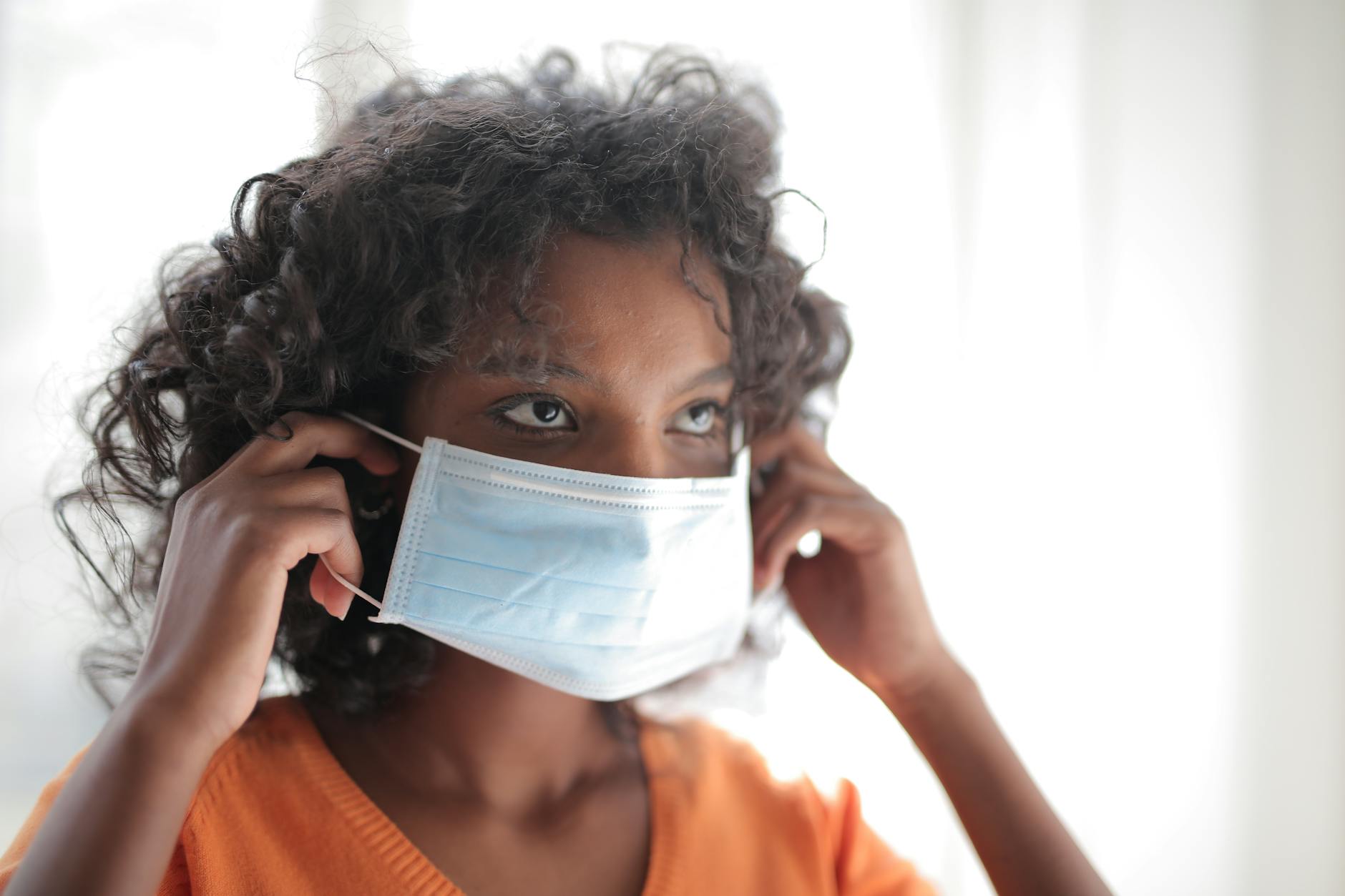 Woman in orange shirt wearing white face mask