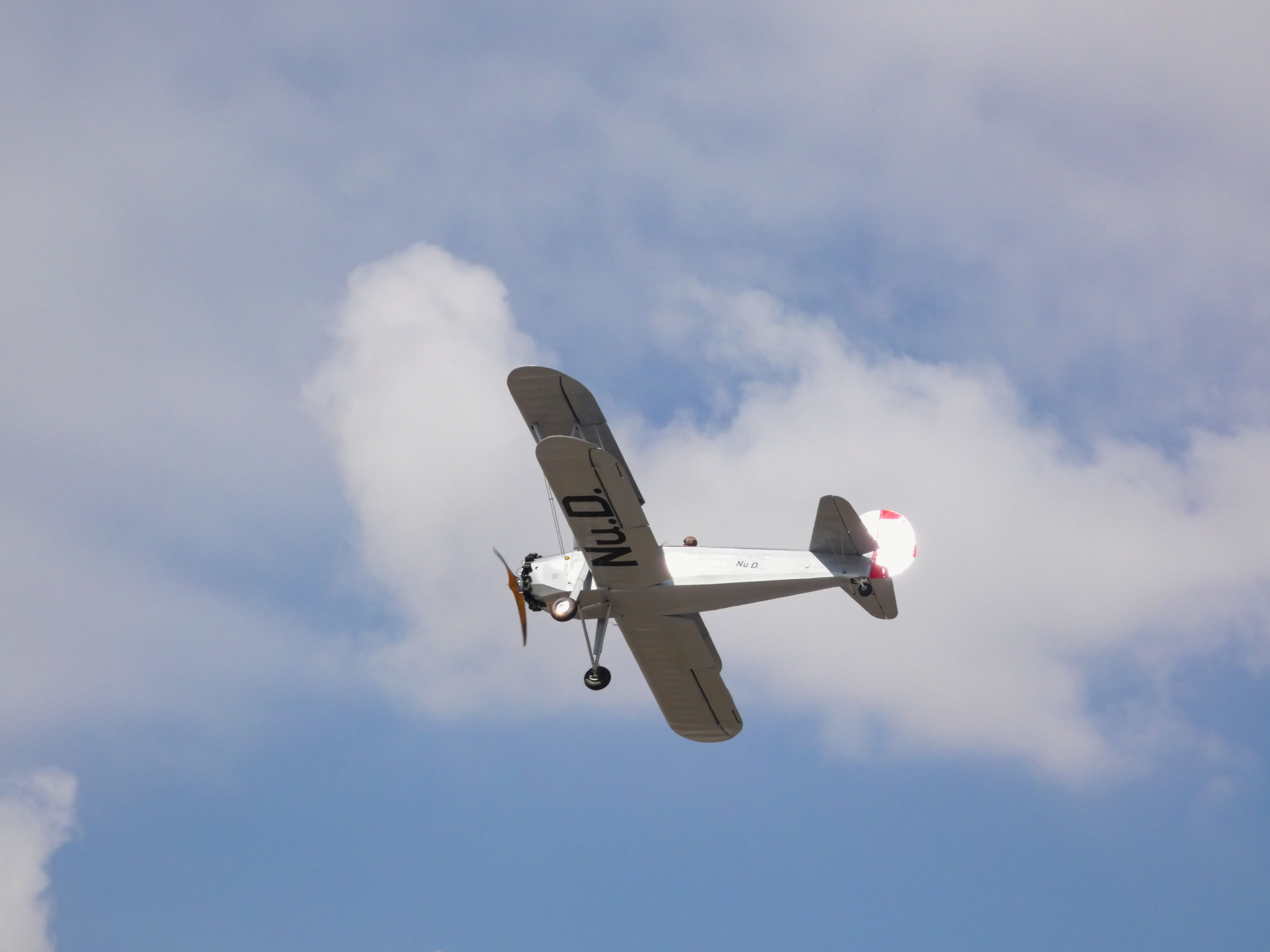 A historic biplane with visible retro markings flying through the clear blue sky during daylight.