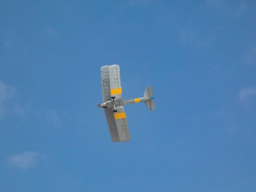 Free A vintage airplane flies against a clear blue sky, showcasing its yellow and grey colors in flight. Stock Photo