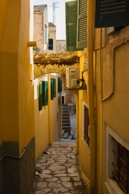 Free Narrow alley in Corfu's old town, showcasing Mediterranean architecture and vibrant yellow walls. Stock Photo