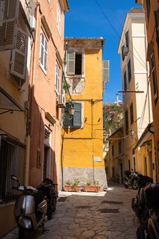 Vibrant narrow alleyway in Corfu with colorful buildings and motorbikes parked along the street.