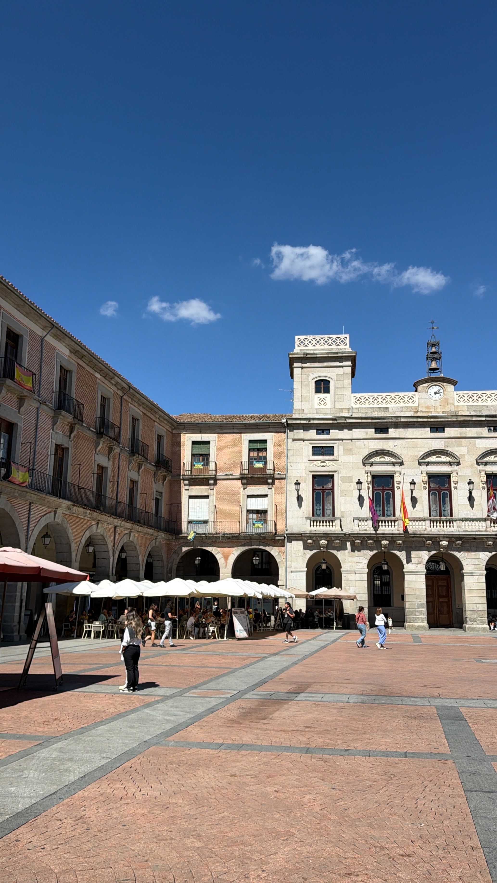 A bustling plaza in Ávila, Spain, featuring historic architecture under a clear blue sky.