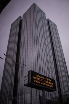 这座高耸的摩天大楼有着玻璃立面，在阴沉的天空下引人注目地矗立于城市景观中