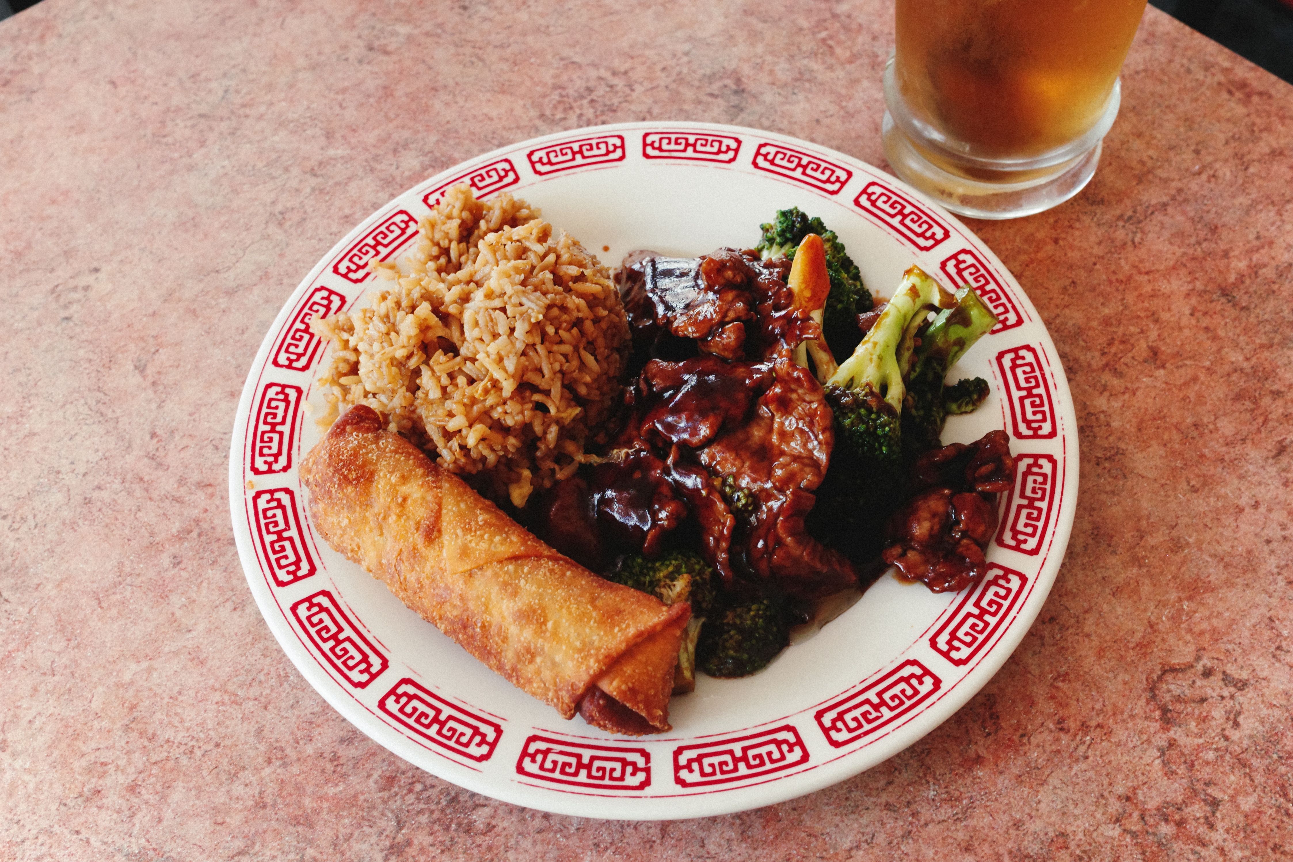 Plate of Chinese food featuring egg roll, fried rice, and beef with broccoli.