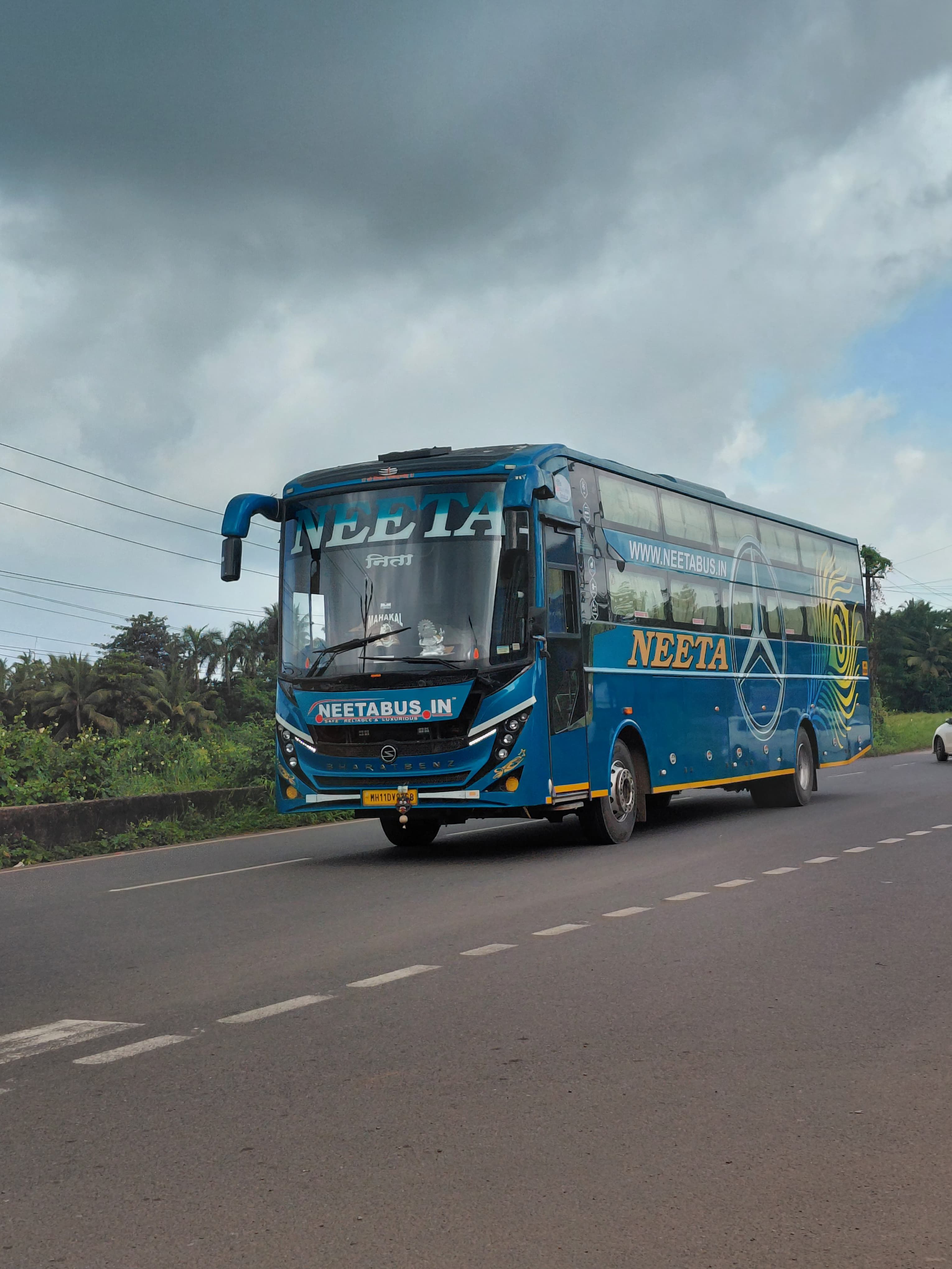 Blue Neeta travel bus on a highway with cloudy skies and lush greenery around.