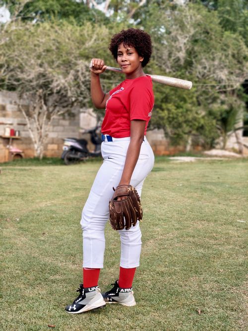 Free Young woman with bat and glove poses confidently outdoors, embodying sportsmanship and casual style. Stock Photo