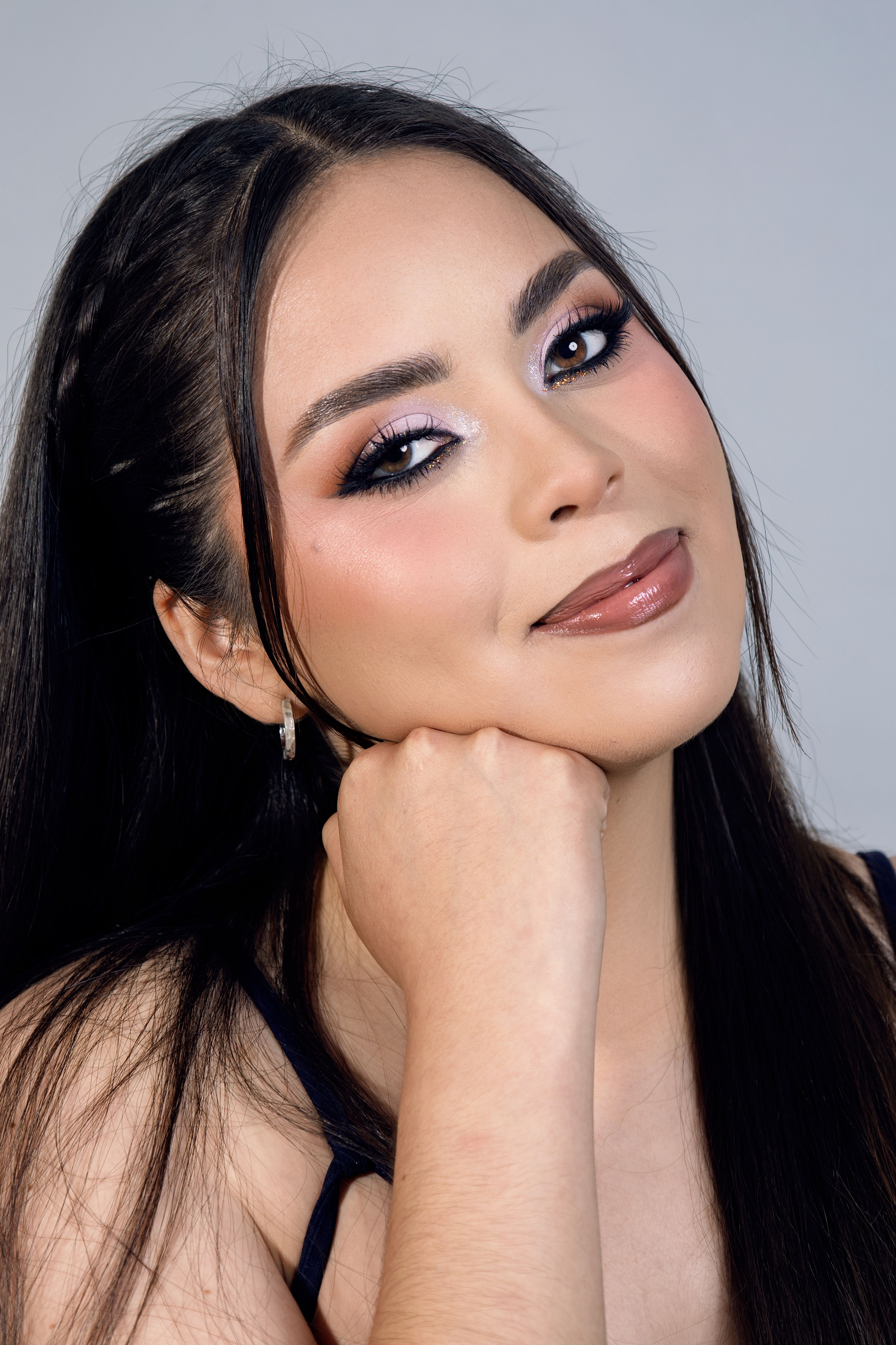 Close-up portrait of a young woman with elegant makeup, posing with a hand under her chin.
