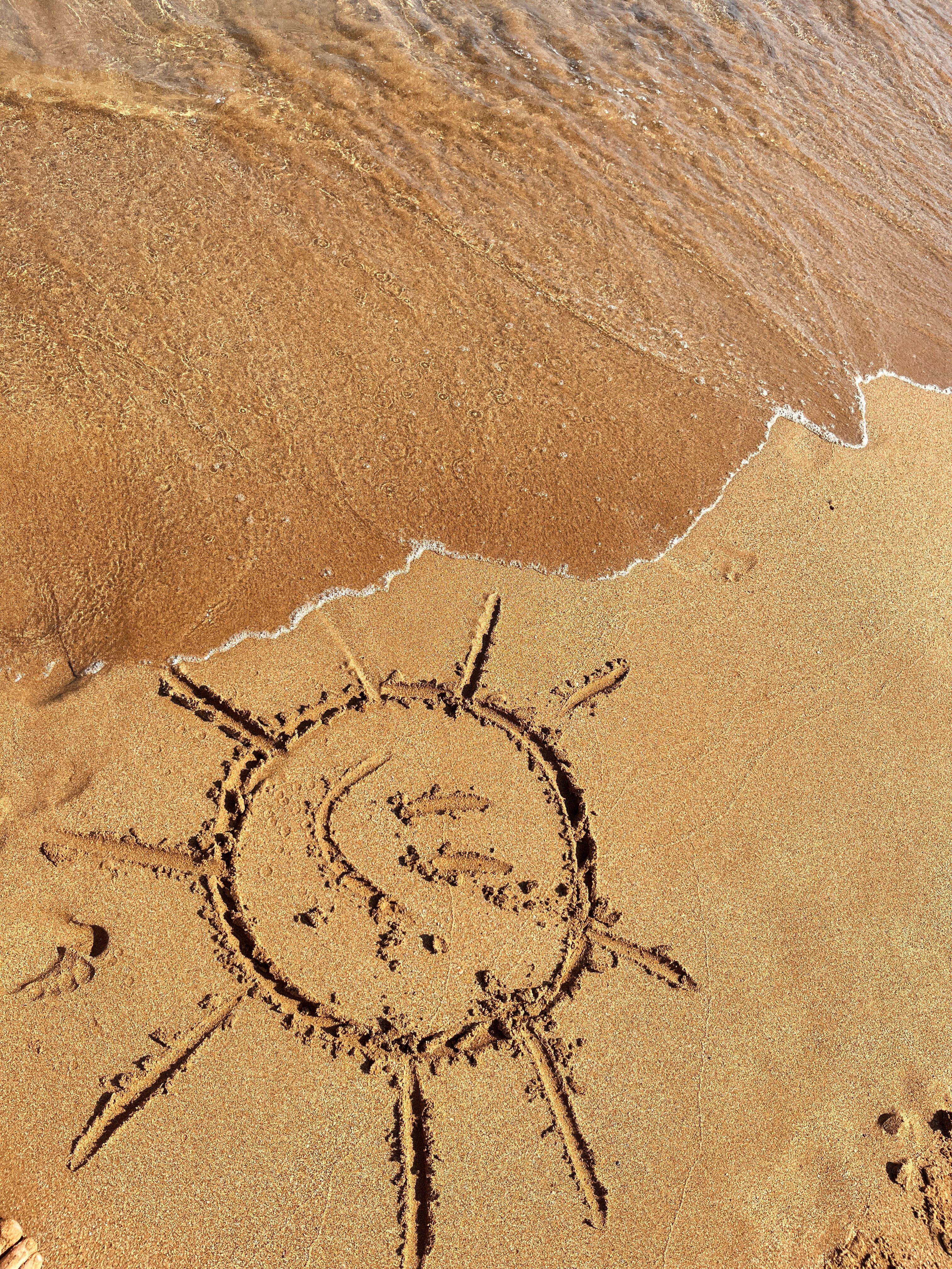 A sun drawing on wet sand as gentle waves approach, creating a serene coastal scene.
