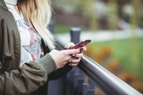 Free Close-up of a woman using a smartphone outdoors, wearing a casual jacket. Stock Photo