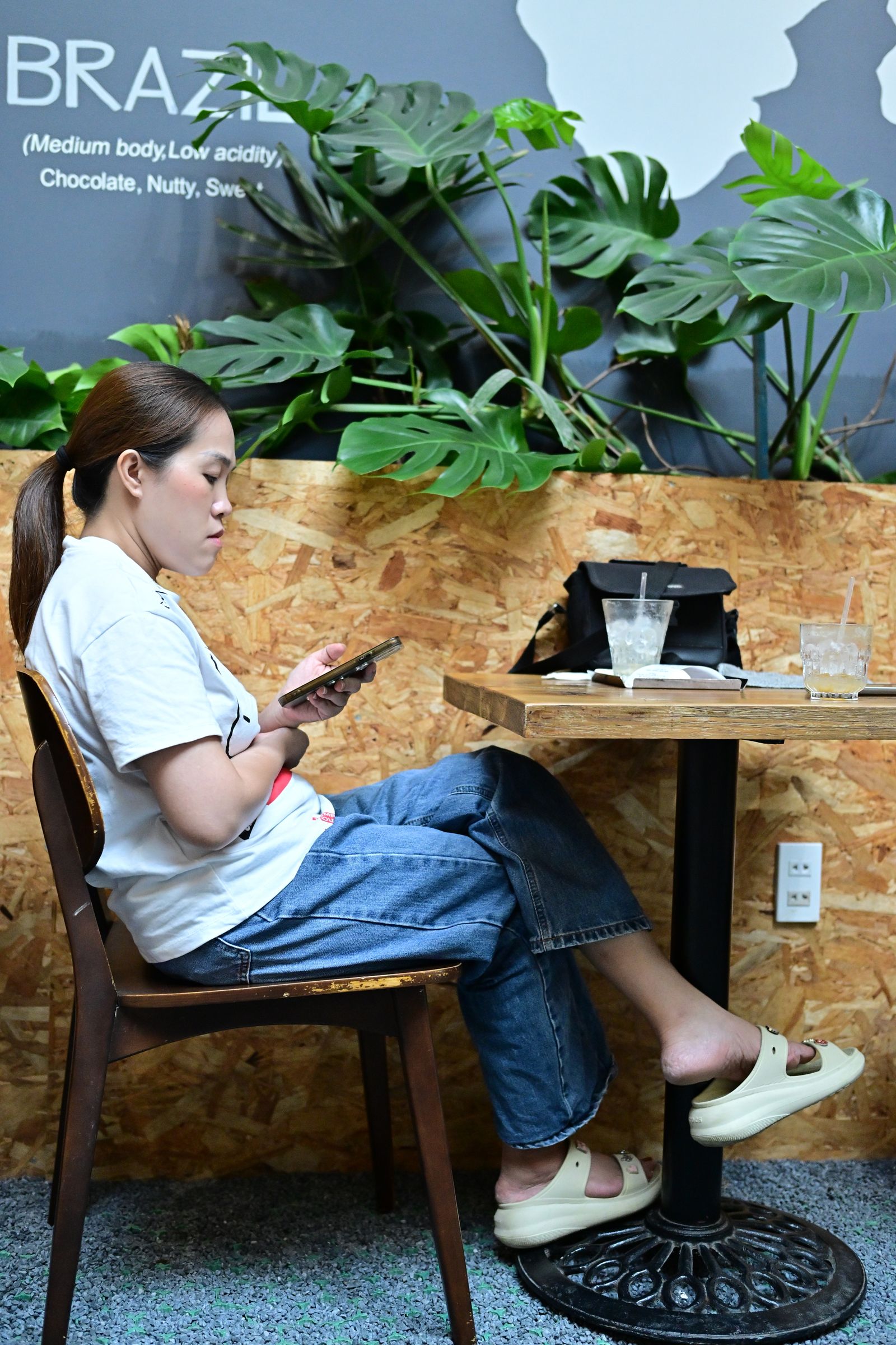 A woman checking her phone in a cafe filled with green plants