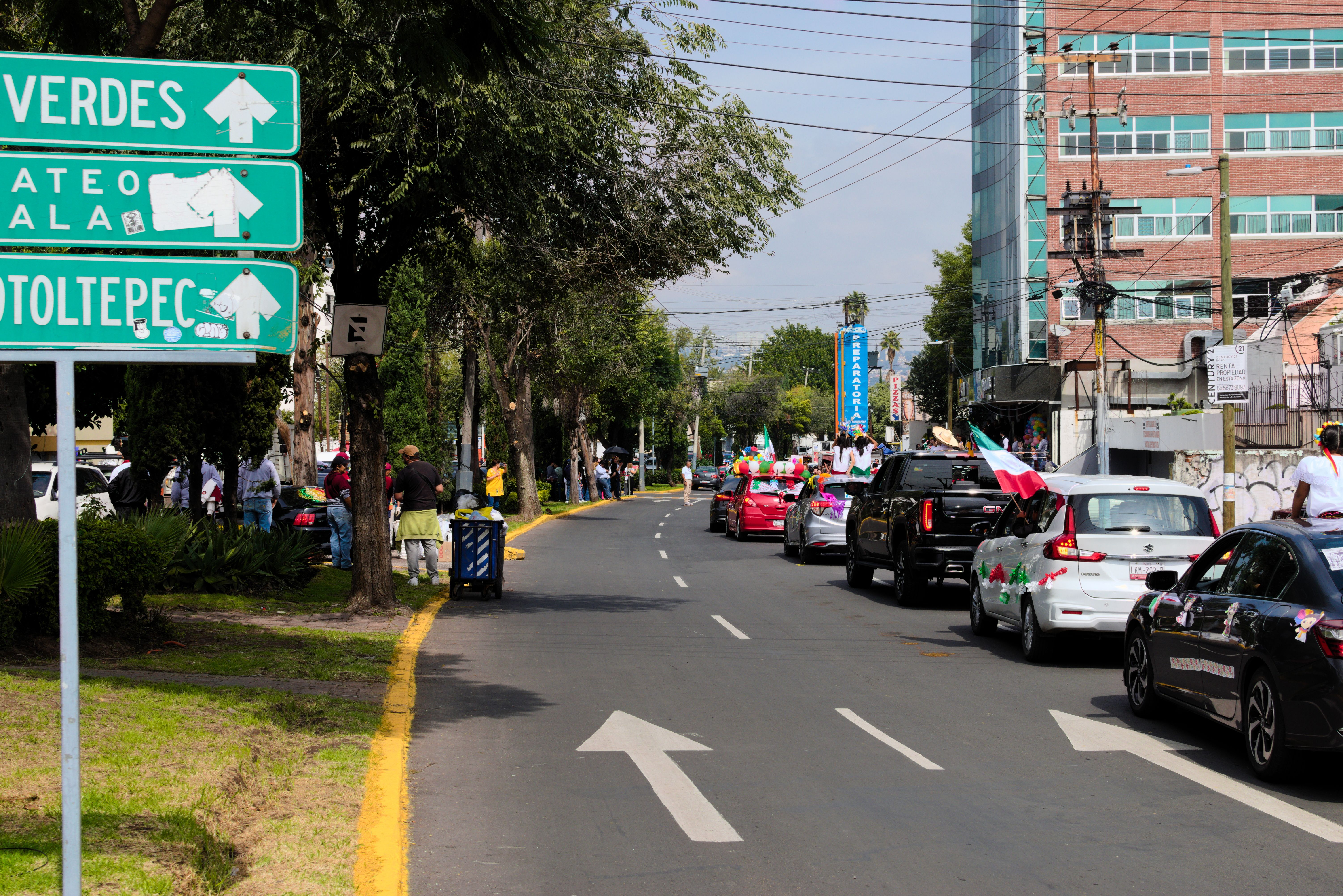 Parade with decorated cars on a city street, next to street signs and modern buildings.