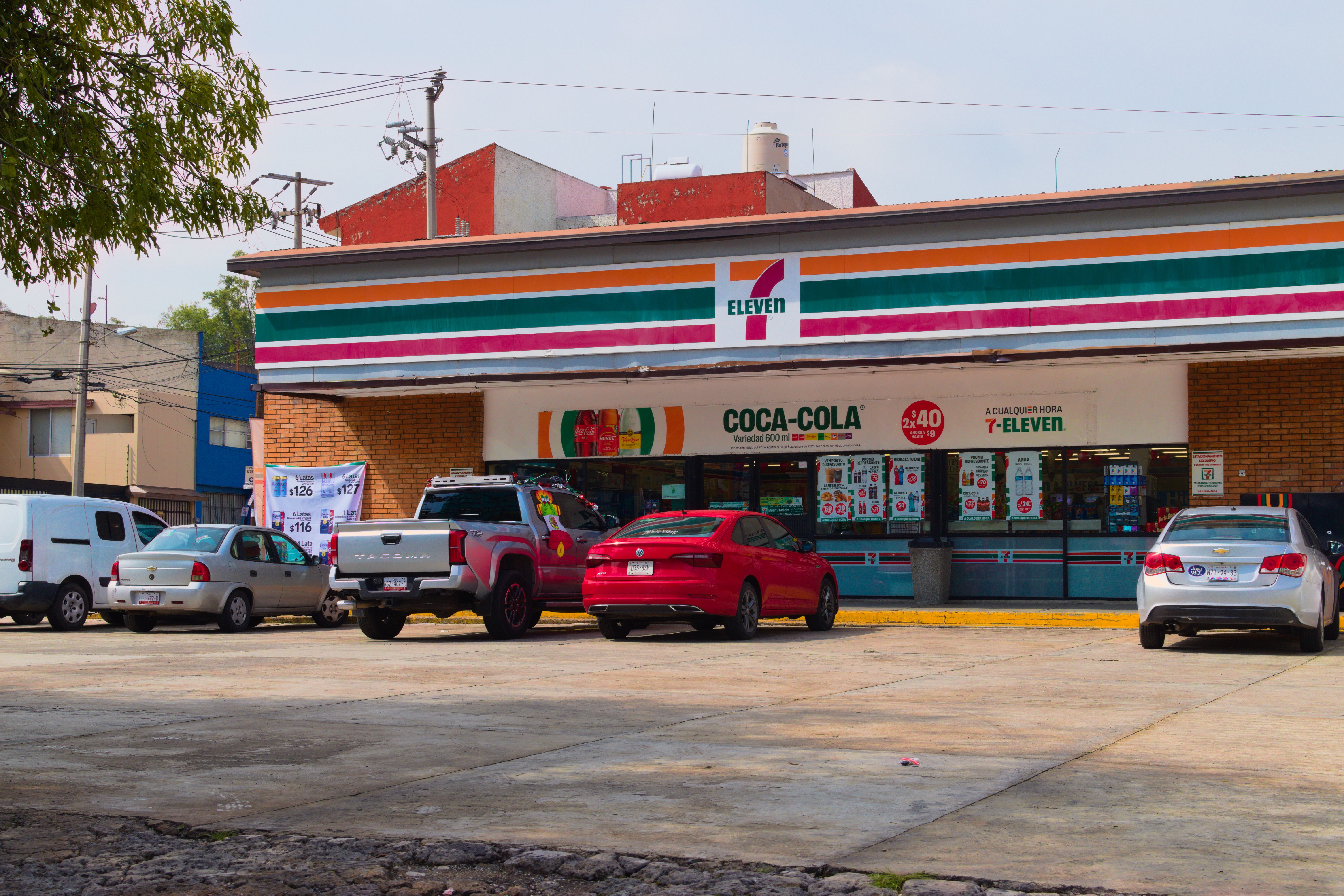 Exterior view of a 7-Eleven store with several cars parked outside under a clear sky.