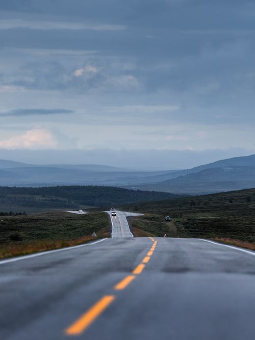 Free Long road stretching towards distant mountains under cloudy skies, ideal for travel themes. Stock Photo