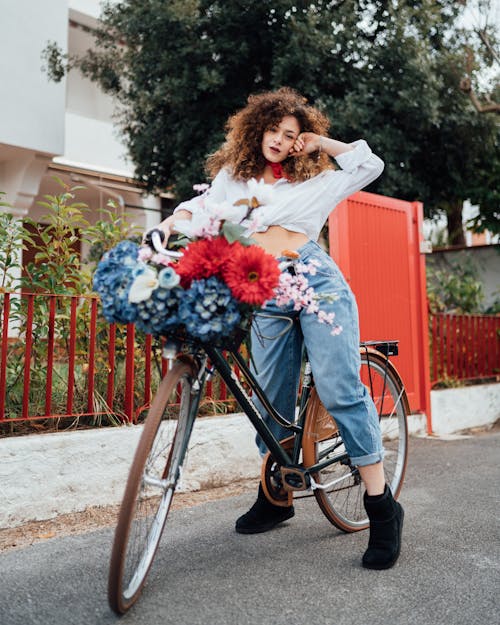 Gratis Mujer En Camisa Blanca De Manga Larga Y Pantalones Vaqueros Azules De Pie Con Bicicleta En La Carretera Foto de stock