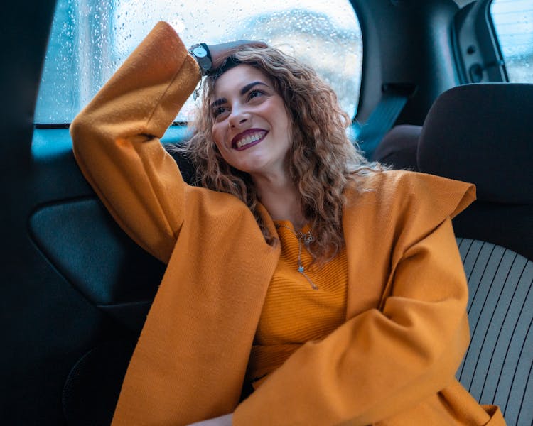 Woman In Orange Coat Sitting On Blue Car Seat