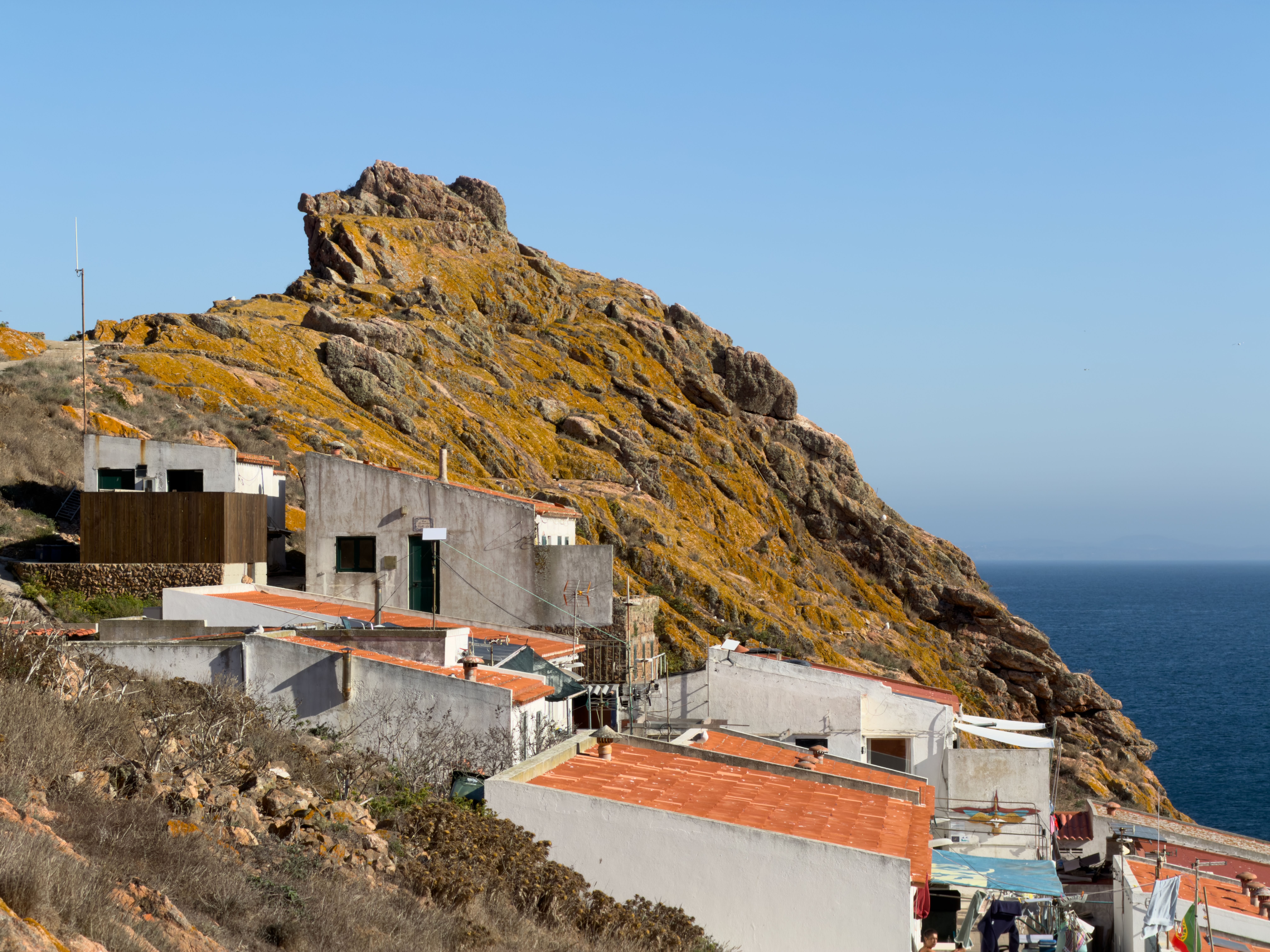 Scenic view of coastal houses against a rugged cliff in Peniche, Portugal, under a clear summer sky.