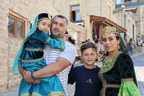 Free A family in vibrant traditional attire poses on a picturesque historic street, showcasing cultural pride. Stock Photo