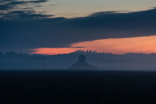 Free Misty rural scene at twilight with a barn silhouette and colorful sky. Stock Photo