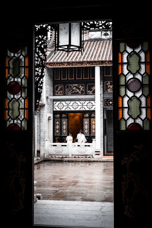 Free View of a traditional Chinese courtyard through ornate stained glass doors showcasing historic architecture. Stock Photo