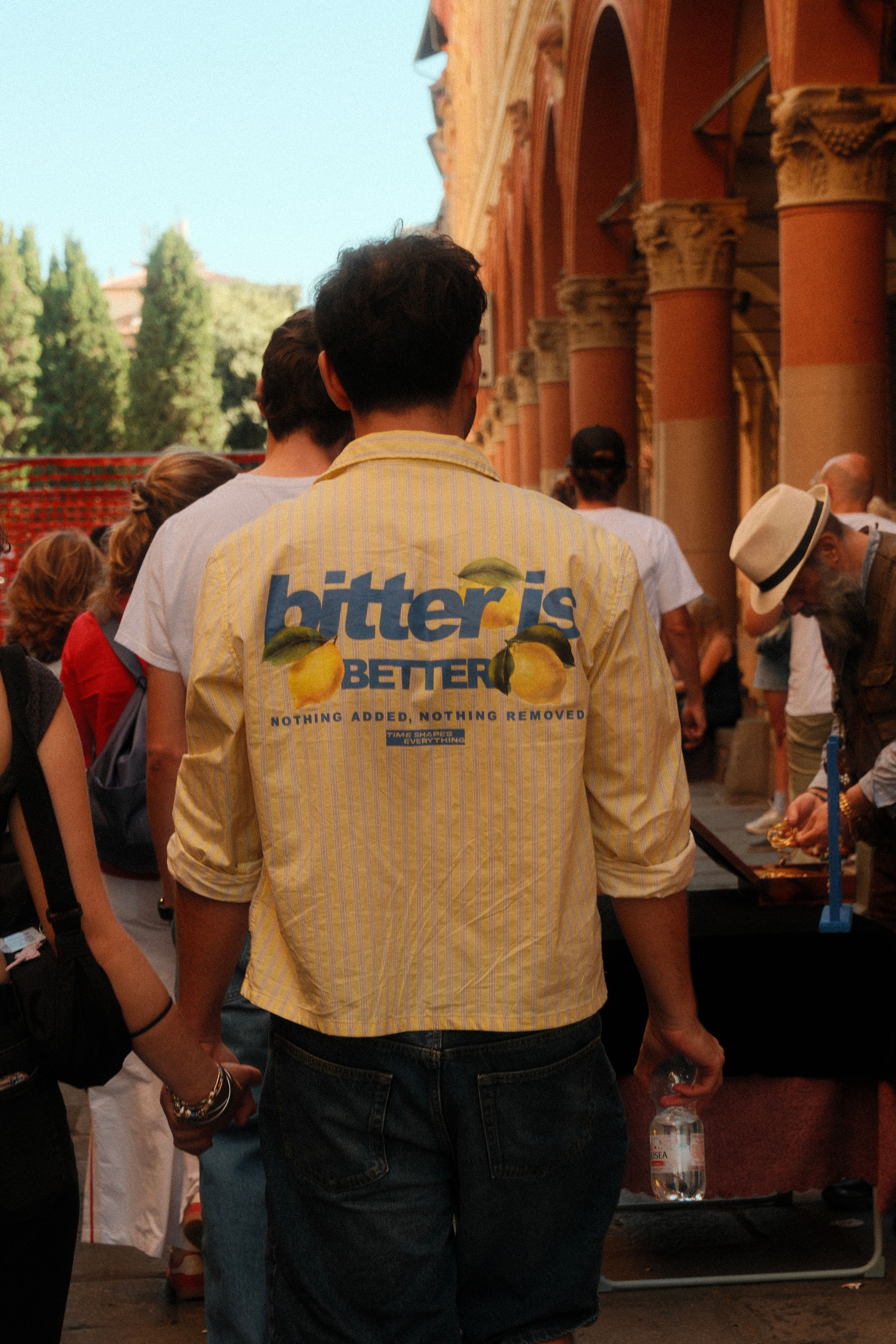 A man walking in Bologna, Italy, wearing a shirt with 'bitter is better' text, emphasizing casual fashion.