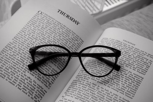 Free Black stylish glasses resting on an open book displaying the word 'Thursday'. Perfect for reading themes. Stock Photo