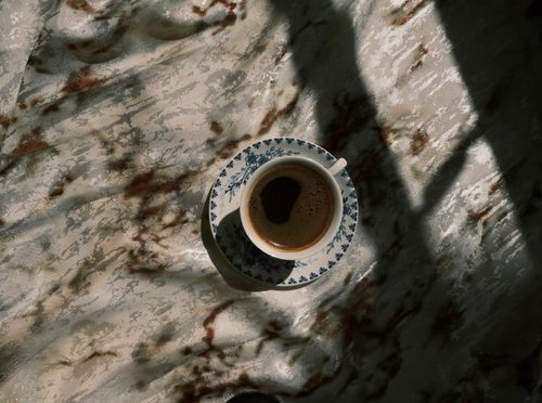 Free A cup of coffee casting artistic shadows on a textured surface, creating a warm, moody ambiance. Stock Photo