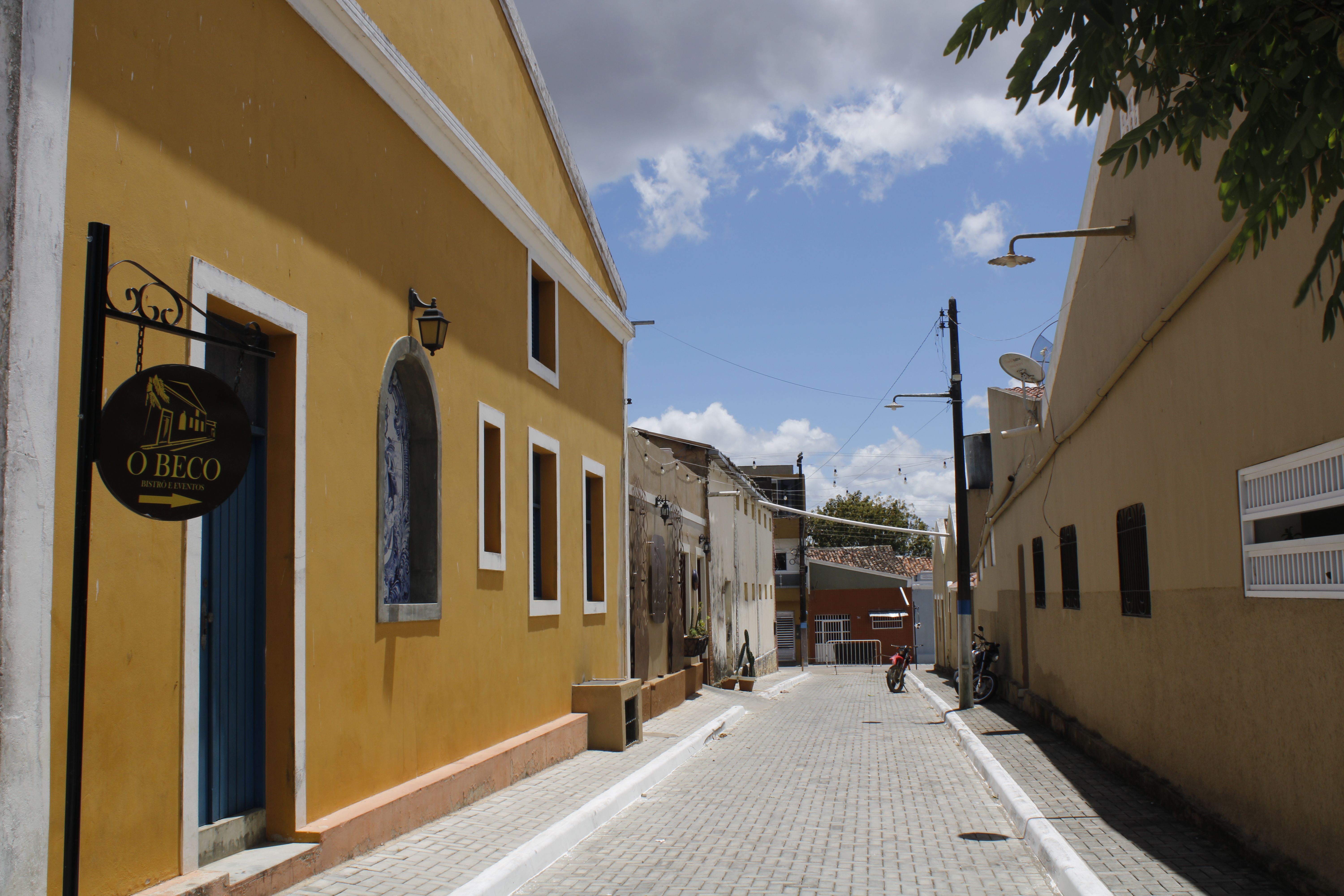 A picturesque alleyway with yellow buildings under a bright blue sky.