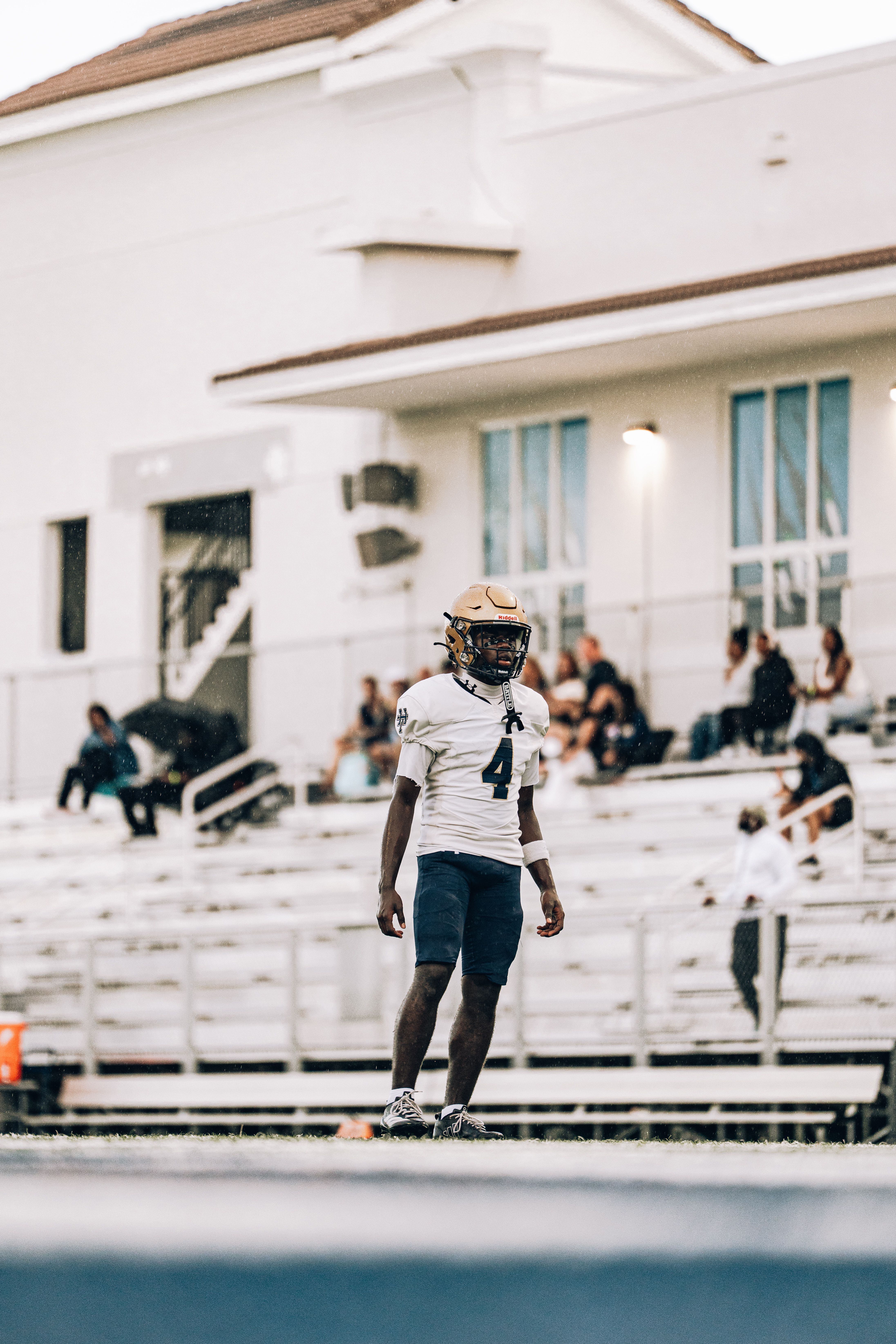 A young football player stands on the field in full gear, ready for a game during the day.