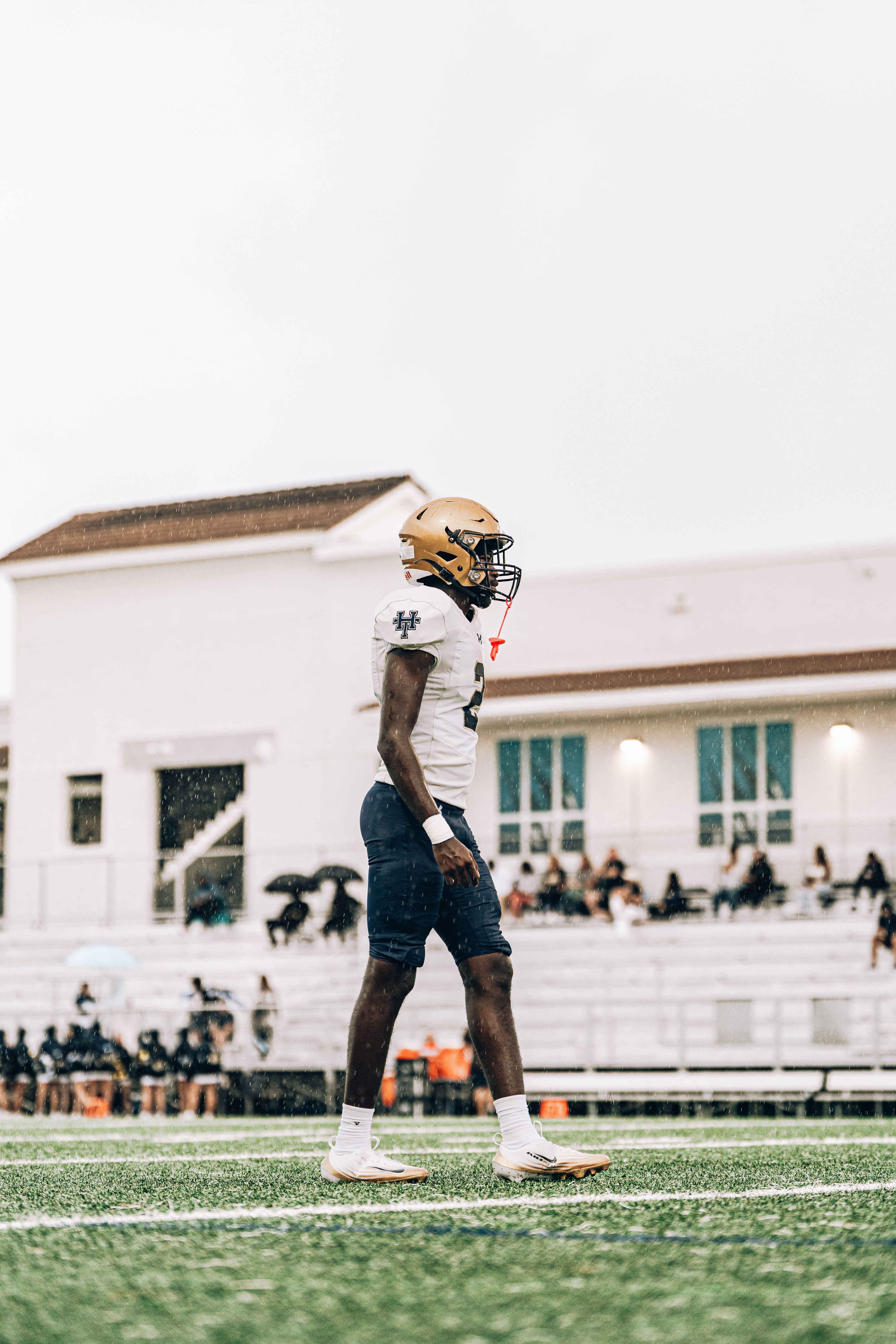A high school football player stands focused on the field during a game.