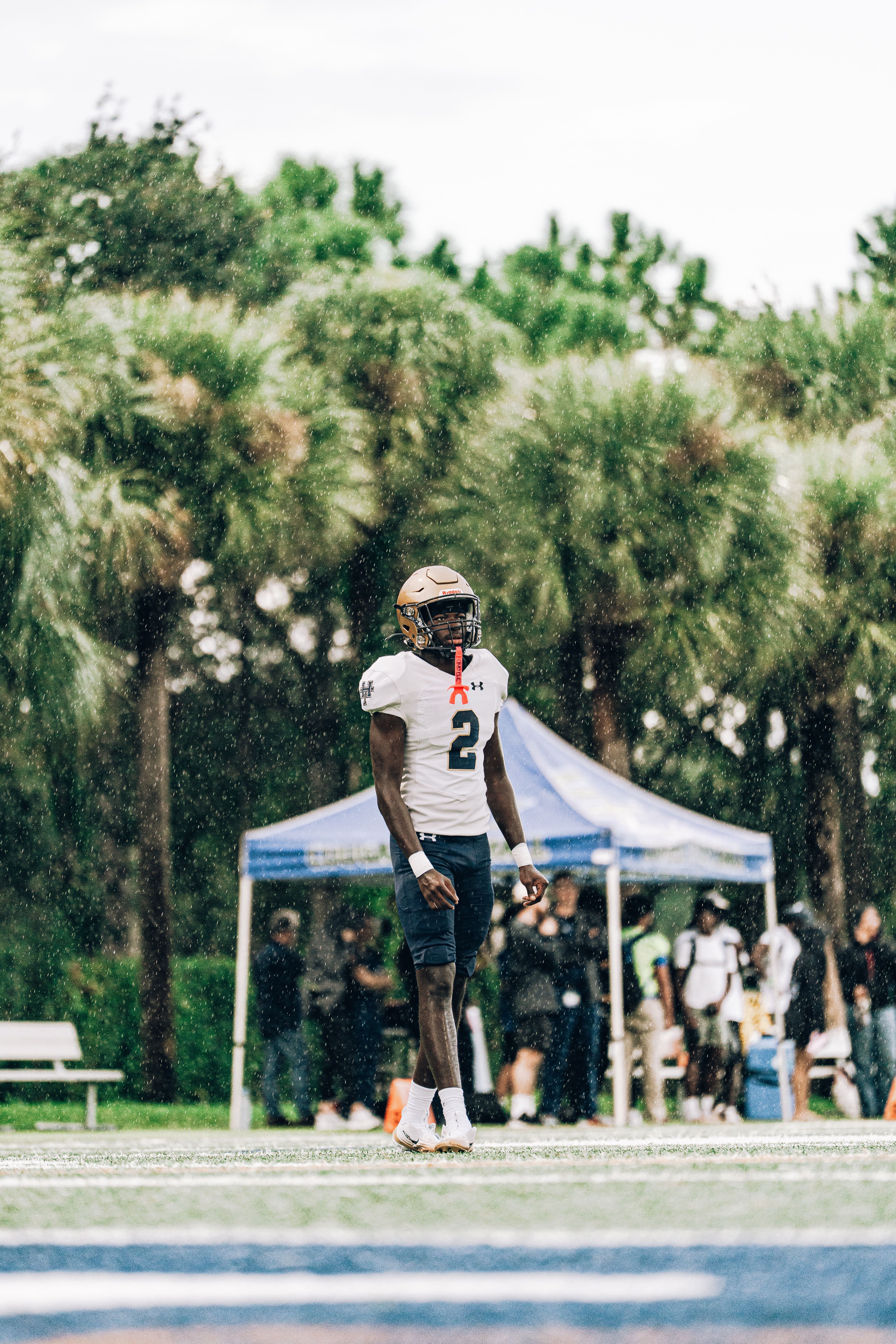 Football player stands in uniform on a rainy field, showcasing determination and focus.