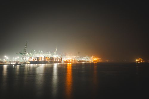 Free Glistening shipping port at night with cargo ships and illuminated cranes reflecting on the water. Stock Photo