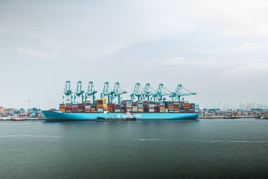A massive shipping vessel loaded with containers docked at a busy industrial port.